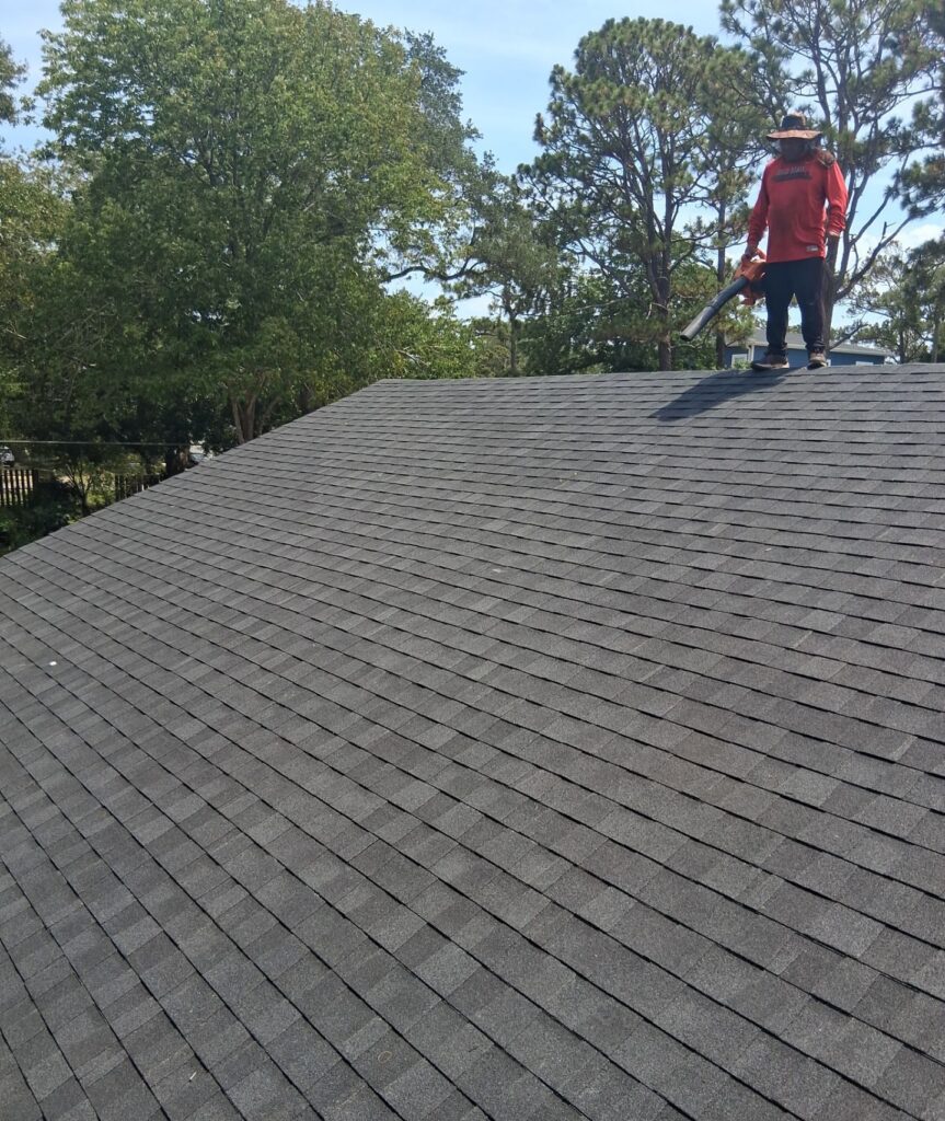 Installed dark shingles along the ridge with a roofer above in Oak Island, NC